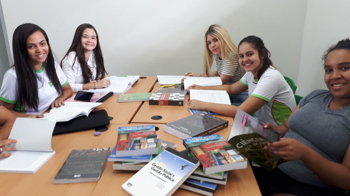 Estudantes sentados ao redor de uma mesa folheando livros